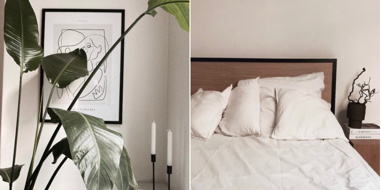 Large plant, drawing in frame on wall, black candle holder with white candles. Wooden bed frame with black edge, white bedsheets and side table with vase